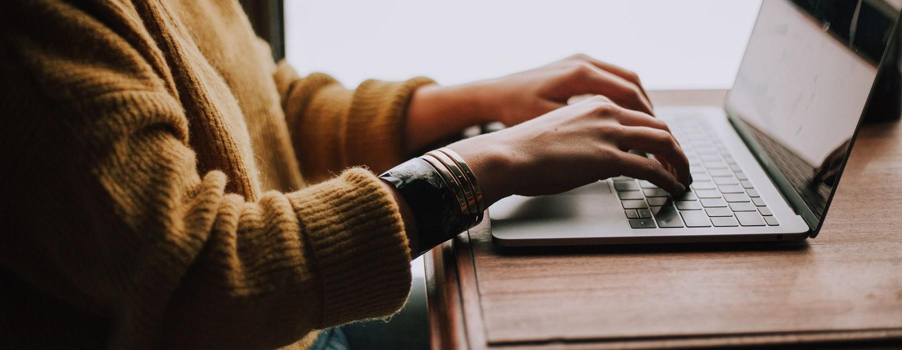 woman types on her laptop near large window